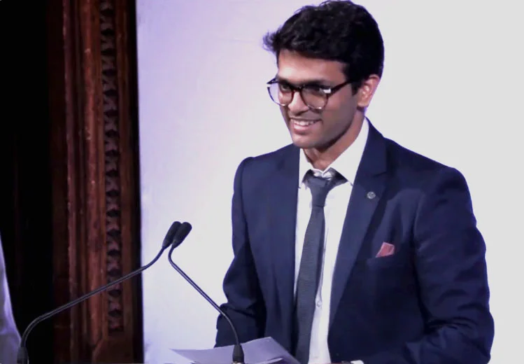 Sid Sethi, Specscart’s founder, delivering a speech at the podium in a navy suit and tie during the Venture Further Awards 2023, with wood panelling and stage lights in the background.