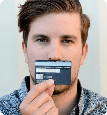 A man holding a credit card horizontally below his nose and covering his mouth, demonstrating a common method for scaling or measuring facial features for glasses.